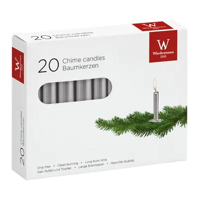 A box of silver chime candles with a sprig of pine needles and a single lit candle.