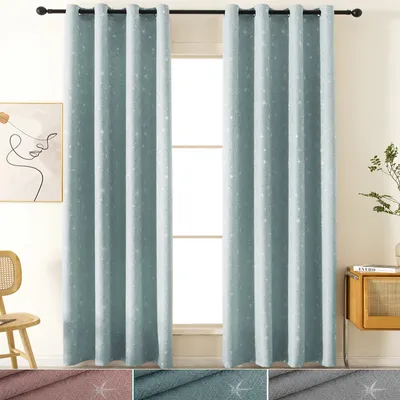 Two blue curtains with a subtle star pattern are hanging on a black curtain rod in front of a window. A chair and a piece of art are visible to the left, and a cabinet with a plant is on the right.
