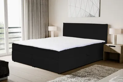 A black boxspring bed with a white mattress is shown in a bedroom setting.