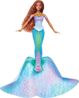 A doll with a mermaid tail and long, wavy brown hair, wearing a purple and blue top and a golden shell necklace.