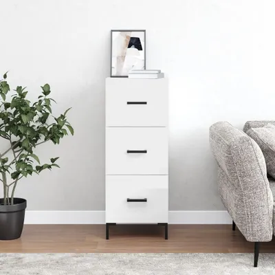 A white sideboard with three drawers is shown in a room with a plant and a couch.