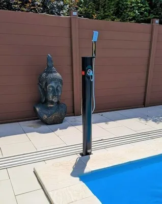 An outdoor shower and a Buddha statue are placed next to a swimming pool.