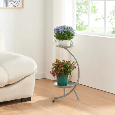 A plant stand with two potted plants next to a sofa and a window.