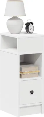 A white bedside table with a lamp and an alarm clock on top, and books and a drawer below.