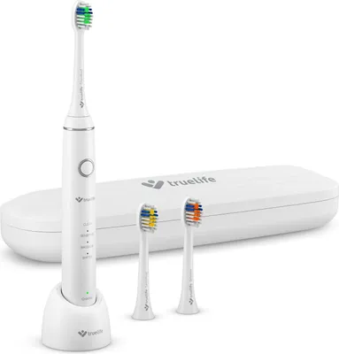 A white electric toothbrush with its charging base and two replacement brush heads, displayed on a white background. A white travel case with the brand logo is also visible.