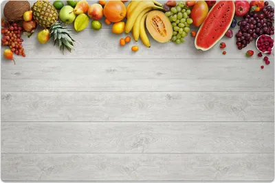 A variety of fresh fruits are arranged at the top of a light gray wooden surface.