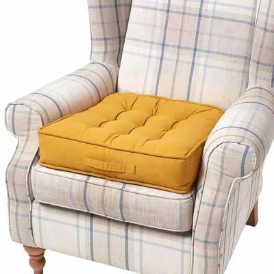 A yellow seat cushion is placed on a plaid armchair.