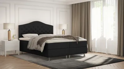 A bedroom scene with a black boxspring bed as the main focus, set against a white wall and light brown curtains.