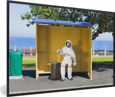 Produktbild von MuchoWow® MuchoWow® Gerahmtes Poster Komischer Astronaut in einem Buswartehäuschen 90x60 cm - Poster mit zchwarzem Bilderrahmen - Fotorahmen - Foto-Plakat