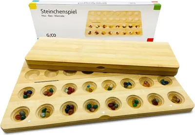 A wooden board game with colorful stones in its pits, with its packaging in the background.