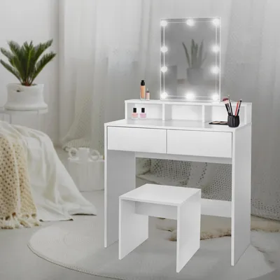 A white vanity table with a lighted mirror and a stool, set up in a bedroom with soft lighting.