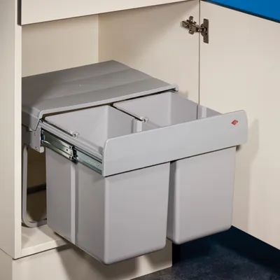 A pull-out trash bin system with two compartments installed inside a kitchen cabinet.