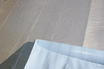 A close-up view of a roll of light blue self-adhesive roofing membrane laid out on a gray surface, with shadows cast by sunlight.