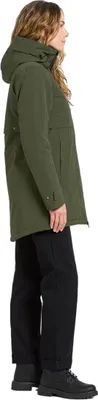 A woman wearing a green parka and black pants, shown from the side.