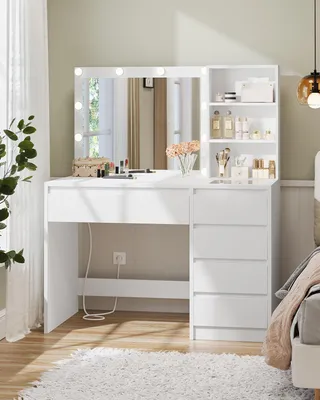 A white vanity table with a lighted mirror and drawers, set up in a bedroom.