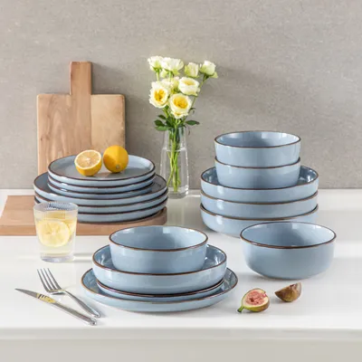 A table setting with a blue ceramic dinnerware set, lemons, figs, and a vase of white flowers.