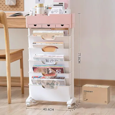 A mobile storage rack with multiple drawers and shelves, filled with books and magazines, is placed next to a wooden desk and chair.