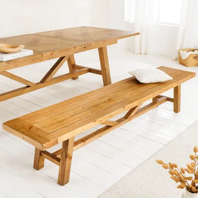 A wooden bench and table set in a bright, airy room with white flooring and sheer curtains.