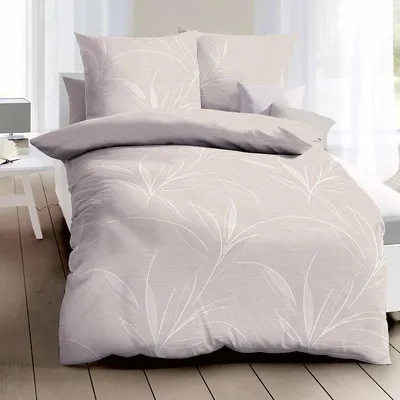 A neatly made bed with beige bedding featuring a white leaf pattern, set against a bright window.
