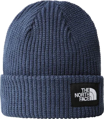 A close-up studio shot of a blue knitted beanie with a black logo patch.