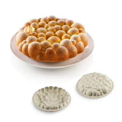A baked cake with a bubble-like texture sits on a white plate, with two silicone molds of the same texture below it, all on a white background.