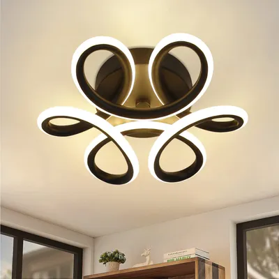 A modern geometric ceiling light fixture with swirling arms, illuminated with warm white LED lights, mounted on a white ceiling.