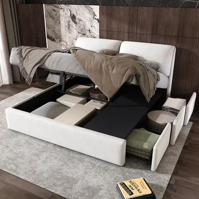 A white upholstered bed frame with its storage drawers and lift-up mattress base open, revealing storage compartments. The bed is made up with blankets and pillows, and is set in a bedroom with a marble and wood paneled headboard.