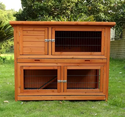 A wooden rabbit hutch with multiple compartments, set up outdoors on a grassy lawn.