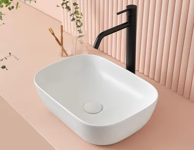 A white washbasin with a black faucet on a pink countertop, with a ribbed pink wall in the background.