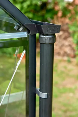 A close-up view of a black downspout attached to a greenhouse.