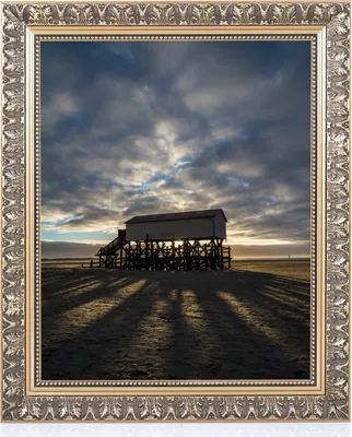 A framed image of a stilt house on a beach at sunset.