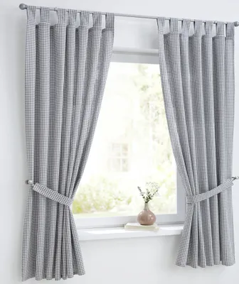 Two curtains are shown hanging on a curtain rod in front of a window. The curtains are tied back with fabric ties. A small vase with flowers sits on the windowsill.
