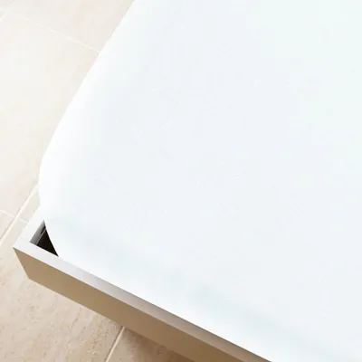 A close-up view of a white fitted sheet on a bed frame.