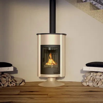 A modern cream-colored wood-burning stove with a black flue pipe, set against a light gray wall. It is flanked by stacks of firewood and white marble-topped side tables with black cushions.
