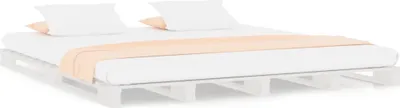 A bed frame made of wooden pallets with a mattress, pillows, and a blanket.