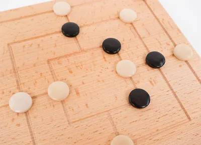 A close-up, angled view of a wooden board game with black and white playing pieces.