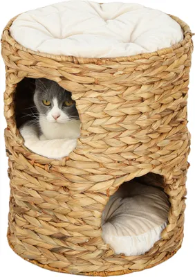 A cat tower made of woven material with two openings and a cushion on top. A cat is visible in one of the openings.