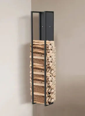 A tall, narrow metal firewood rack filled with logs, standing in a corner against a wall.
