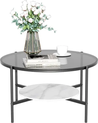 A round coffee table with a glass top and a marble shelf below, decorated with a vase of flowers and books.