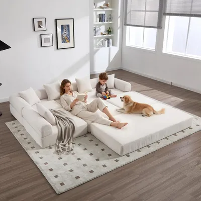 A woman reads a book on a modular sofa while a child plays nearby and a dog rests on the floor.
