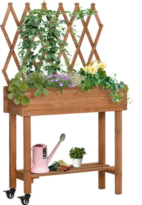 A wooden planter box with a trellis, filled with various plants and flowers, sits on a shelf with gardening tools and a watering can below. The planter has wheels.