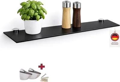 A black glass shelf mounted on a white wall, displaying a potted plant and two spice grinders. Below the shelf, there are mounting brackets and screws.