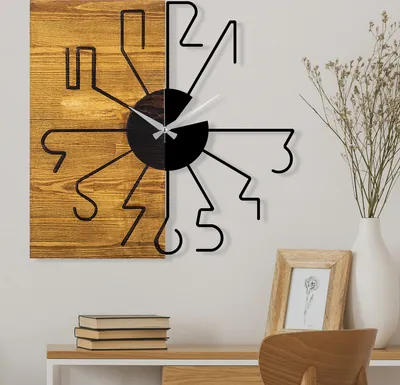 A modern wall clock with a wooden and black design is displayed on a wall above a desk with books and a framed picture.