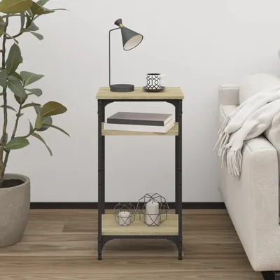 A narrow console table with two shelves, a lamp, a mug, books, and decorative candles, placed next to a sofa and a plant.