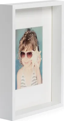 A white shadow box frame with a photo of a young girl wearing sunglasses and holding a seashell.