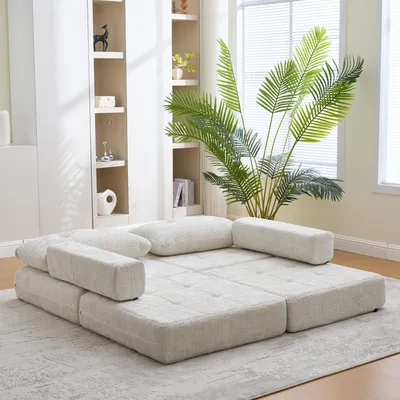 A modular sofa is arranged in a living room setting, with a large plant and bookshelves in the background.