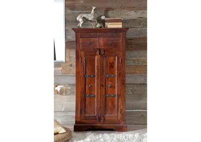 A wooden cabinet with two doors and two drawers, decorated with metal accents, stands against a wooden plank wall. A decorative metal dog and books are on top of the cabinet.