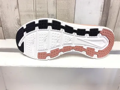The sole of a sneaker is shown against a light-colored wooden background.