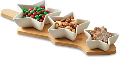 A set of three star-shaped ceramic snack bowls filled with candy, nuts, and cookies, arranged on a wooden tray.