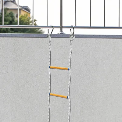 A rope ladder is hanging from a balcony railing, with the wall of the building in the background.